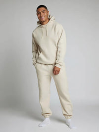 Man wearing a beige hoodie and pants set on a plain background