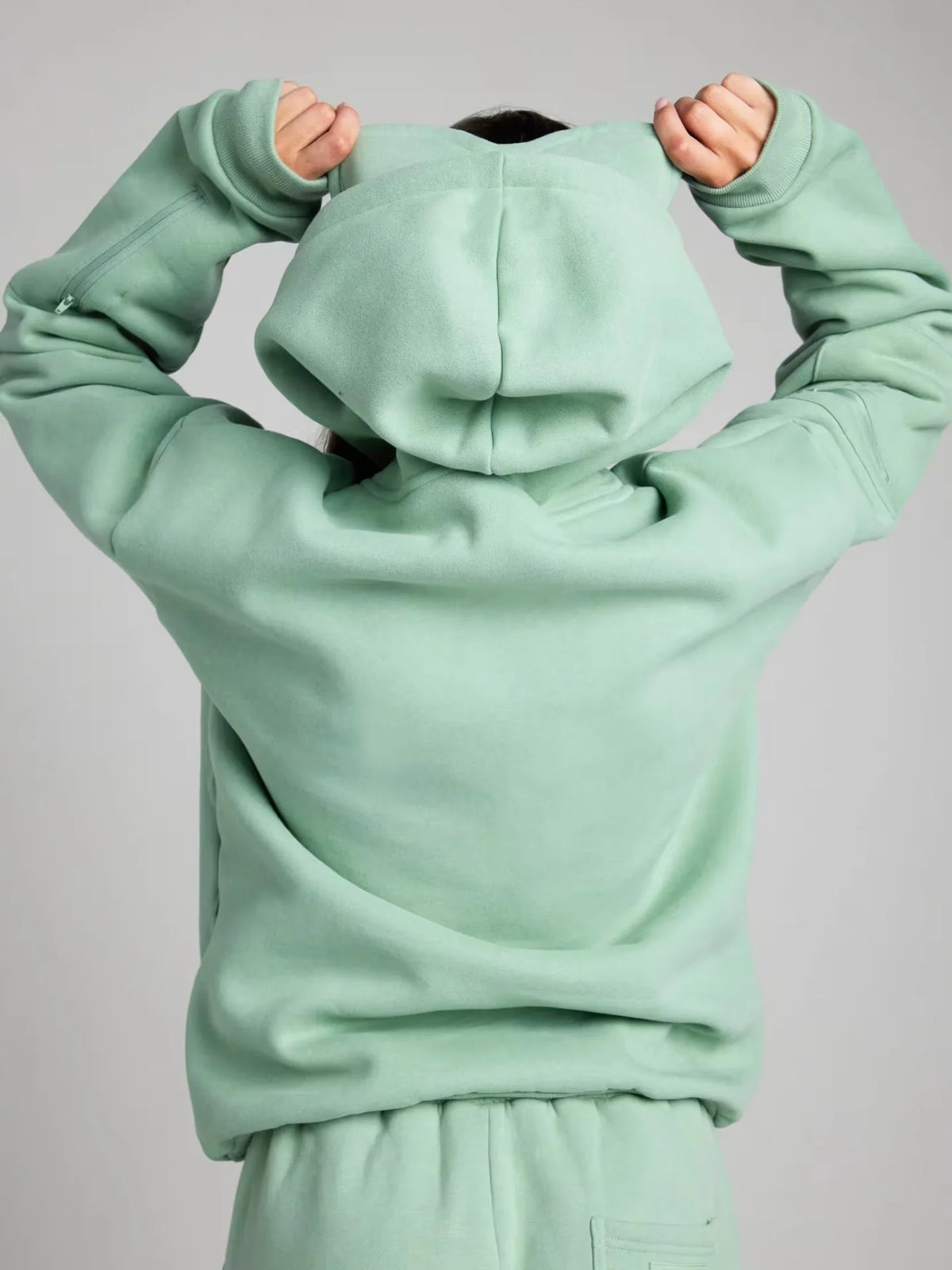 Light green hoodie with a hood held up against a gray background