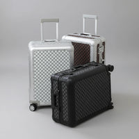 Three suitcases of different sizes on a light-colored floor with a white curtain in the background.