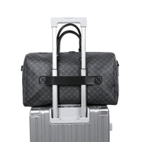 Gray checkered duffel bag with black strap on top of a silver suitcase.
