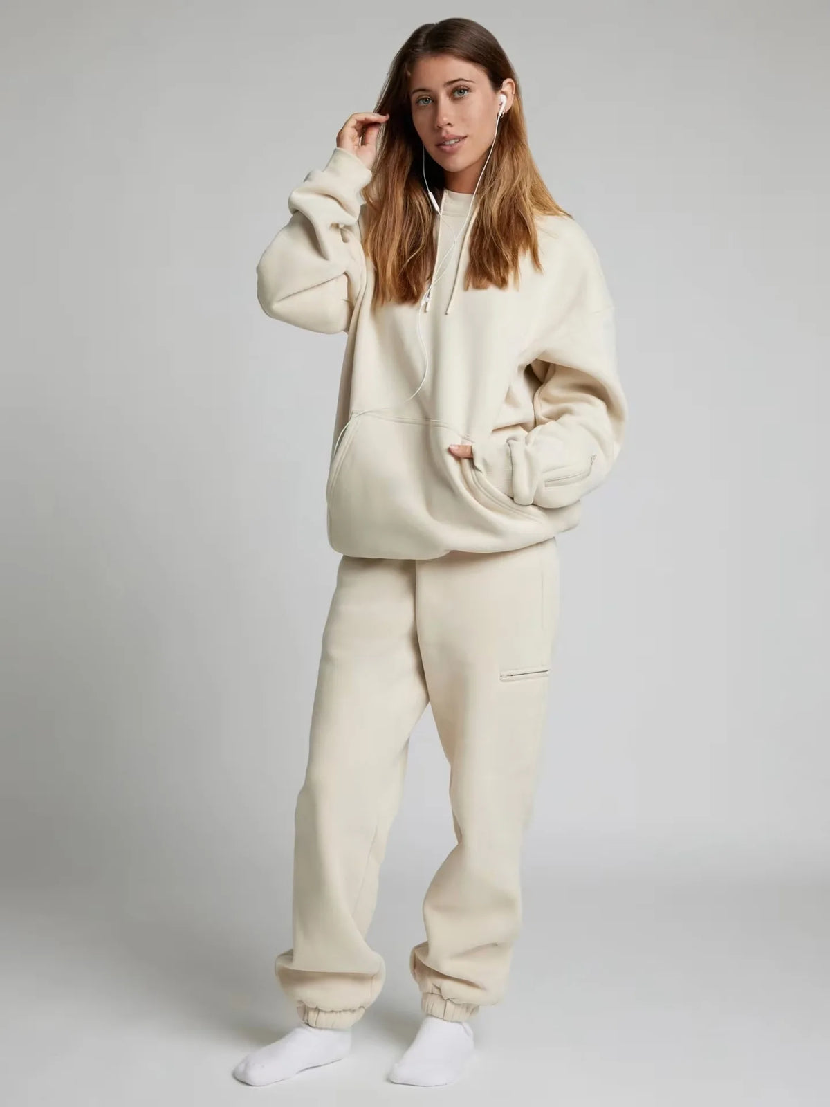 Woman wearing a beige hoodie and pants set on a plain background
