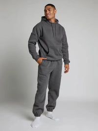 Man wearing a gray hoodie and sweatpants set on a plain background